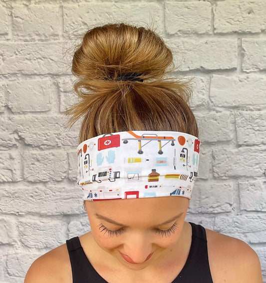 Woman with hair in bun wearing flat, stretchy, white headband with EMT and ambulance theme print.