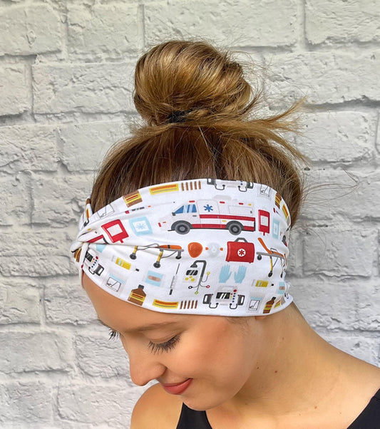 Woman with hair in bun wearing wide, twisted headband in white with ambulance/emergency theme print.
