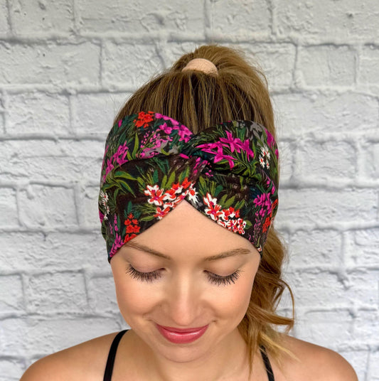 Woman with hair in ponytail wearing wide, twisted headband in black with fuchsia and red/white floral print.