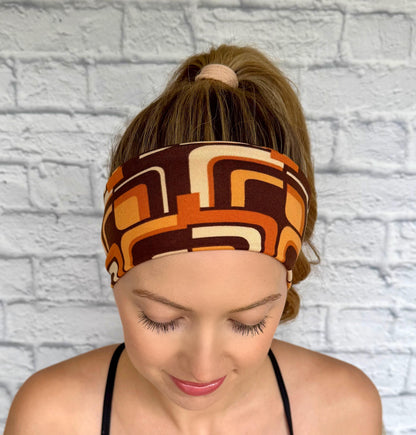 Woman with hair in ponytail wearing flat, stretchy headband in brown and orange retro geometric print.