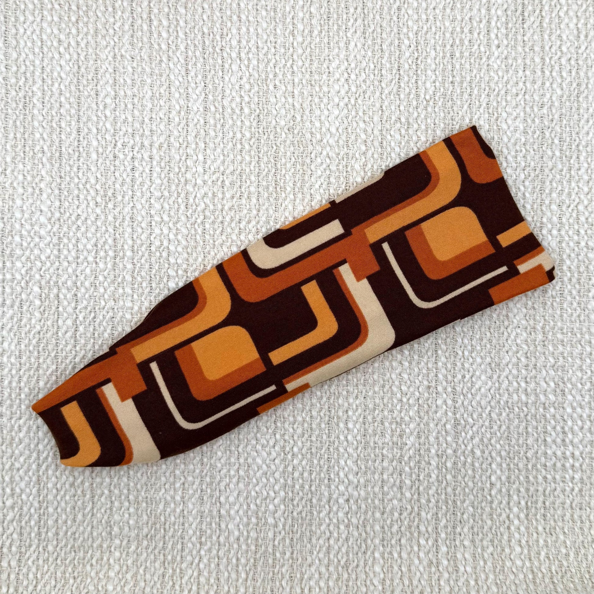 Flat, stretchy headband in brown and orange retro geometric print.