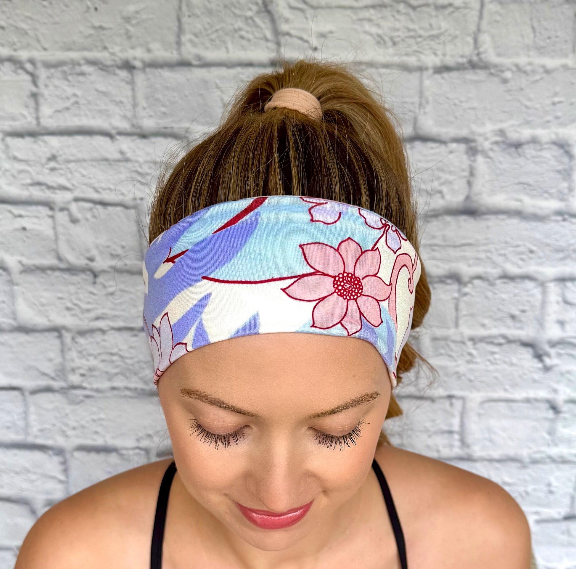 Woman with hair in ponytail wearing flat, stretchy headband in lavender, light blue, pink, and white floral print.
