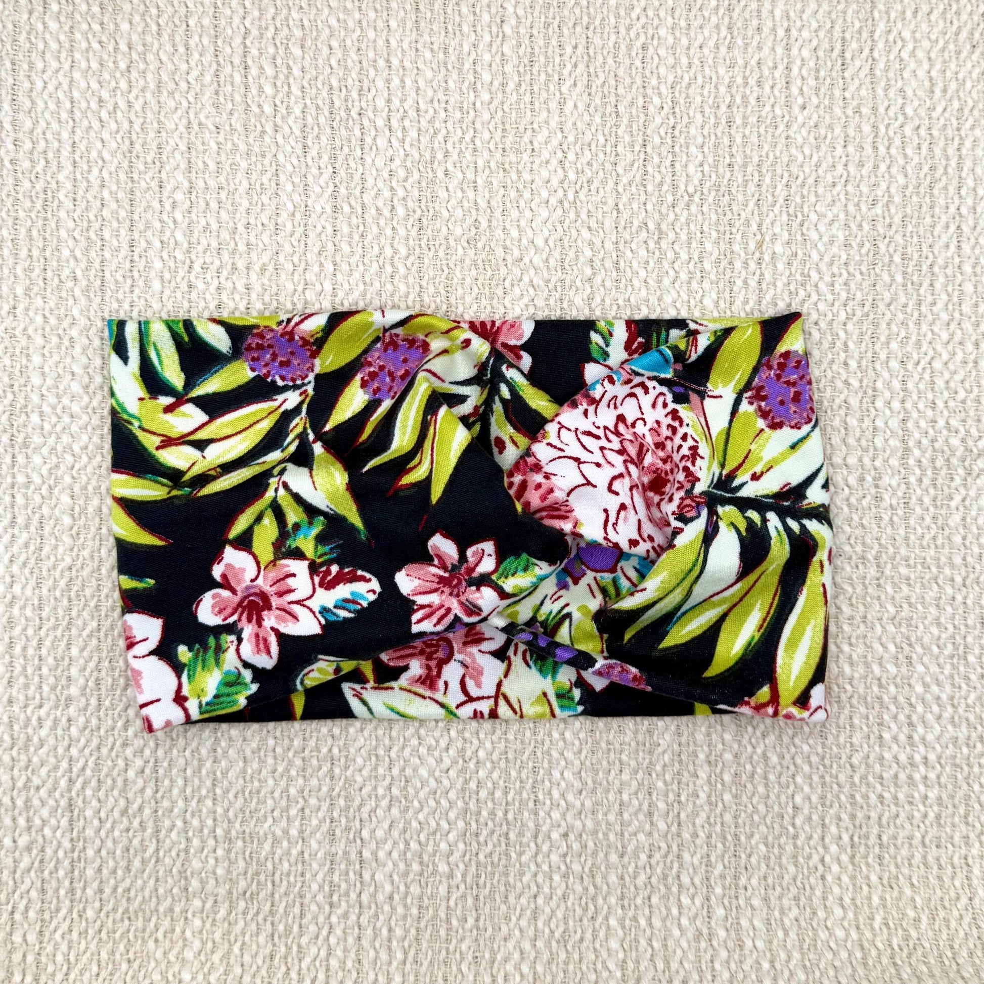 Wide, twisted headband in black with lime green, pink, white, and purple floral print.