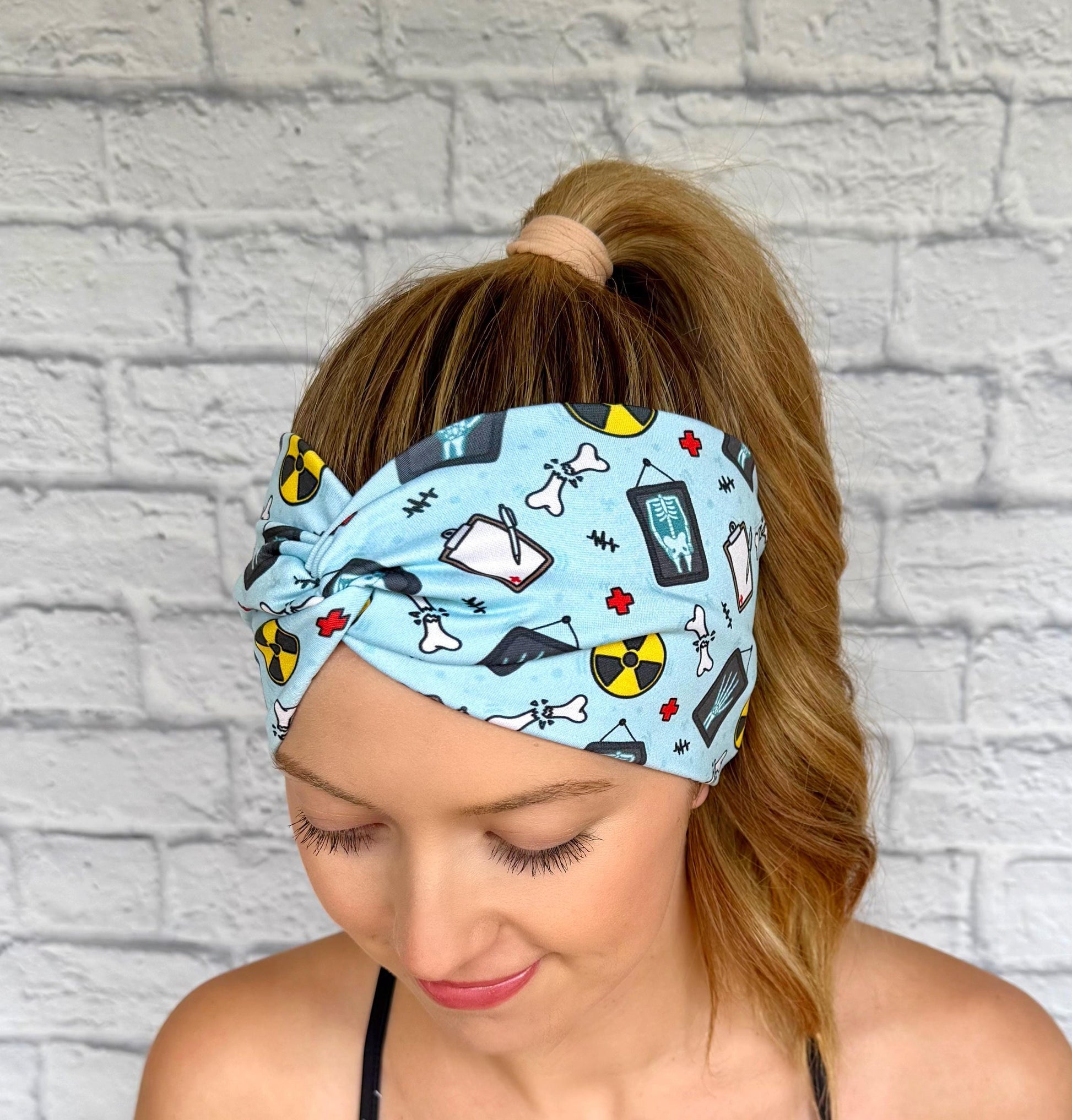 Woman with hair in ponytail wearing wide, twisted, blue headband with radiology theme print.