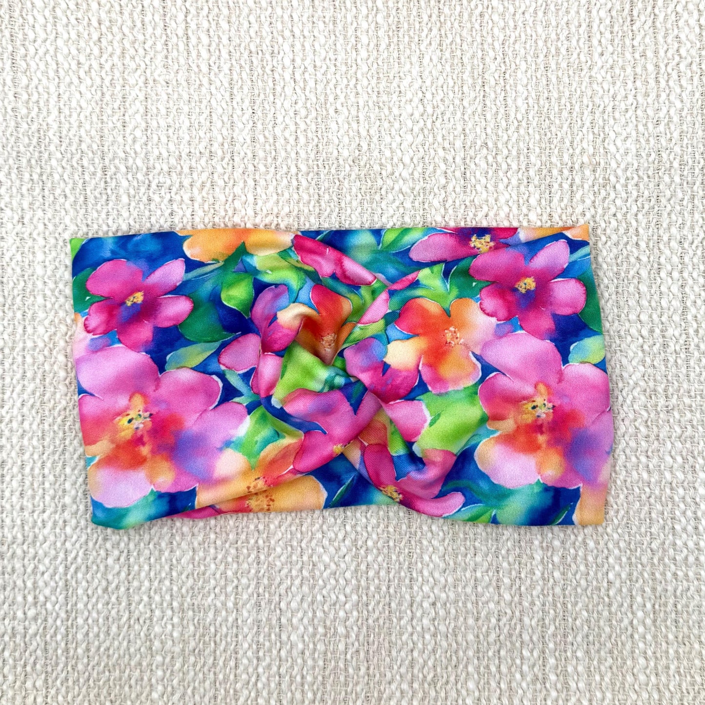 Wide, twisted headband in blue with bright, multi-color Hawaiian theme floral print.