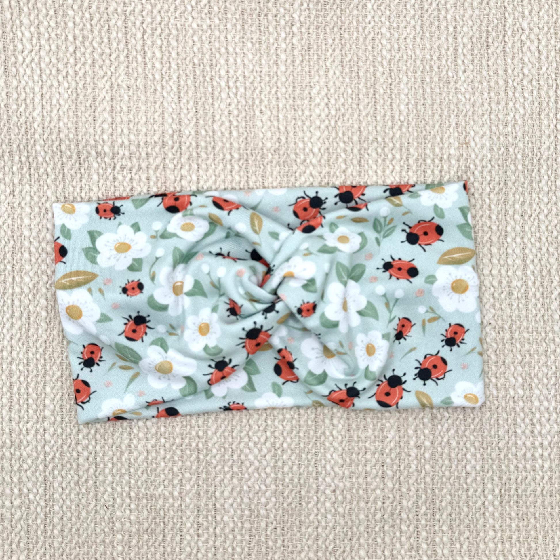 Wide, twisted, light blue headband with ladybug and white floral print.