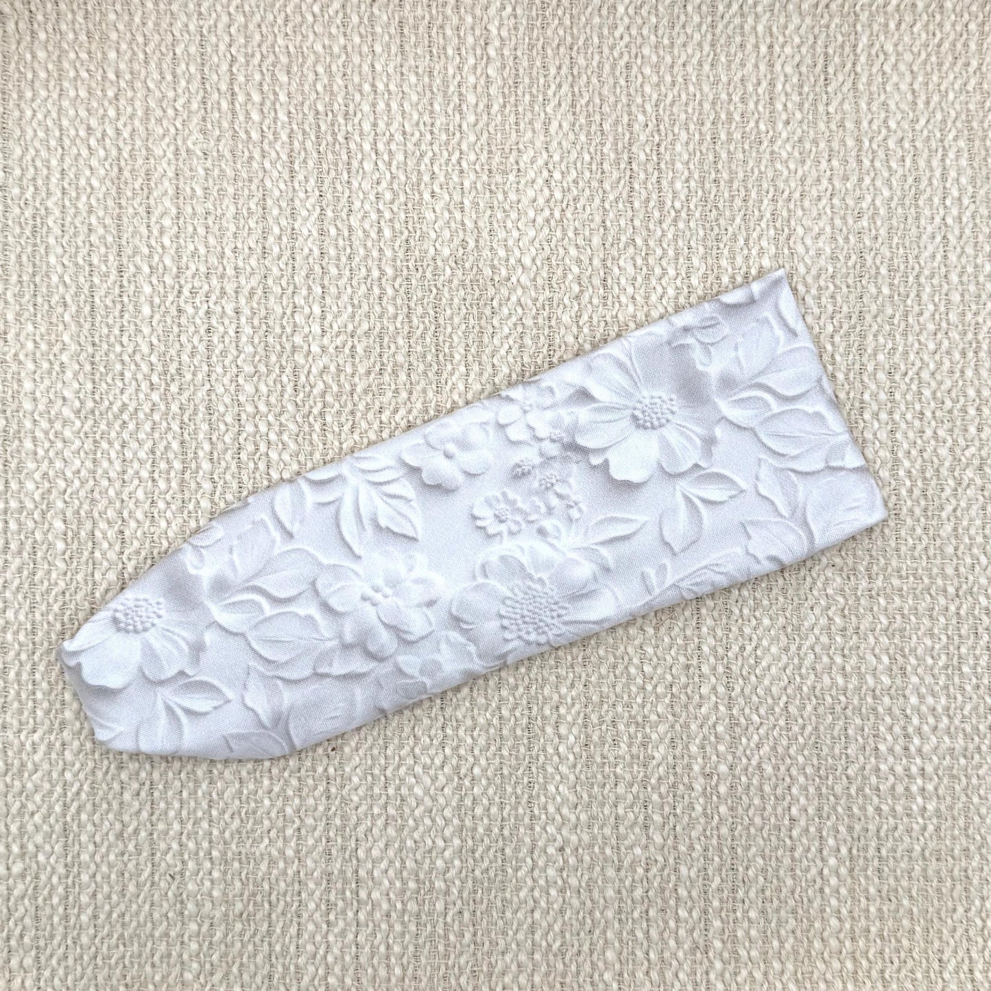 Flat, stretchy, white headband with faux embossed floral print and gray shadowing.