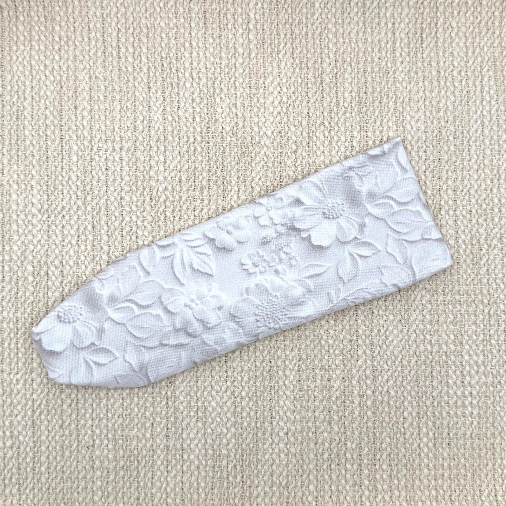 Flat, stretchy, white headband with faux embossed floral print and gray shadowing.