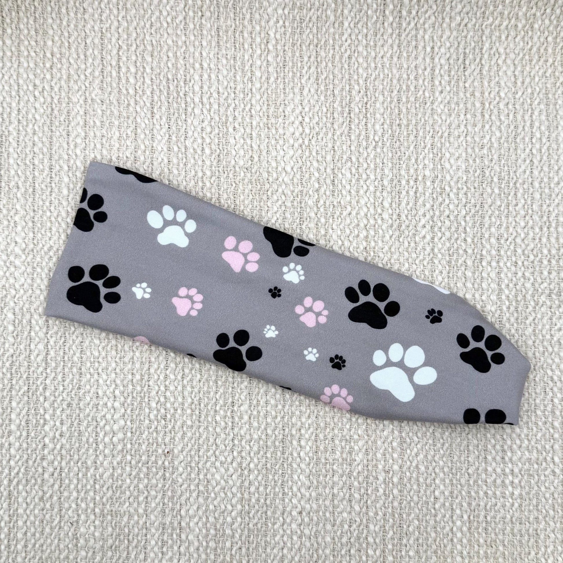 Flat, stretchy headband in gray with white, pink, and black dog paw print.