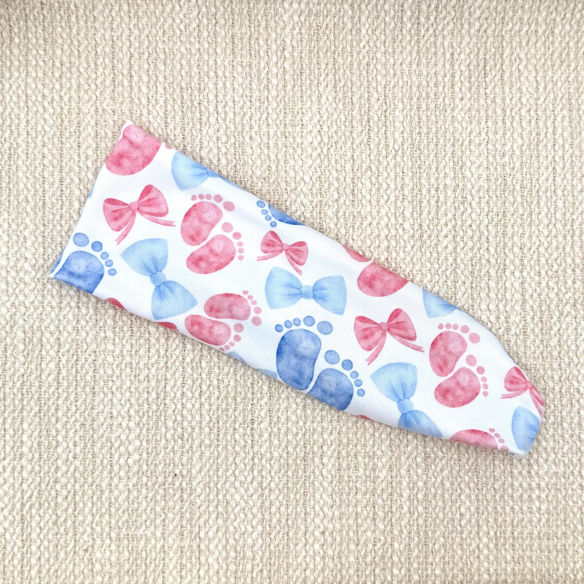 Flat, stretchy, white headband with pink and blue baby feet and bow print.