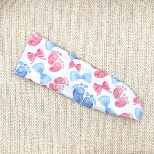 Flat, stretchy, white headband with pink and blue baby feet and bow print.