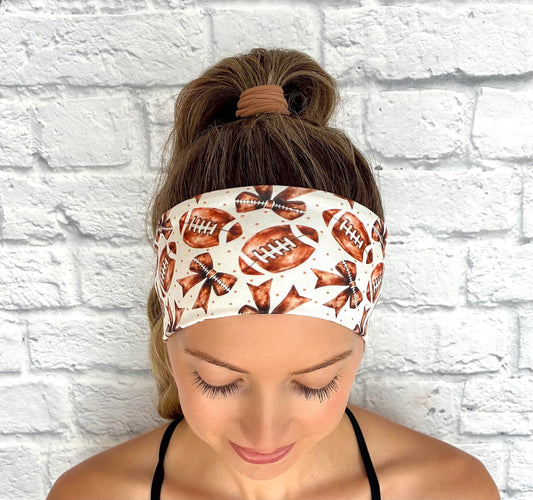 Woman with hair in ponytail wearing flat, stretchy headband in white with brown football and bow print.