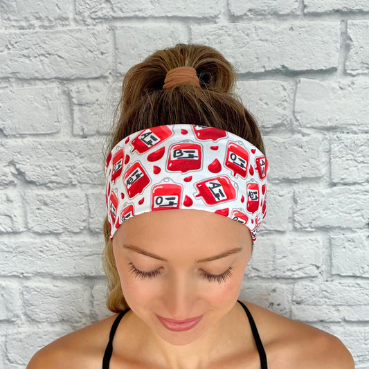 Woman with hair in ponytail wearing white headband with phlebotomy theme print.