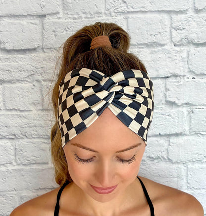 Woman with hair in ponytail wearing wide, stretchy headband in black and tan checker print.