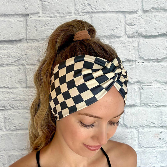 Woman with hair in ponytail wearing wide, stretchy headband in black and tan checker print.