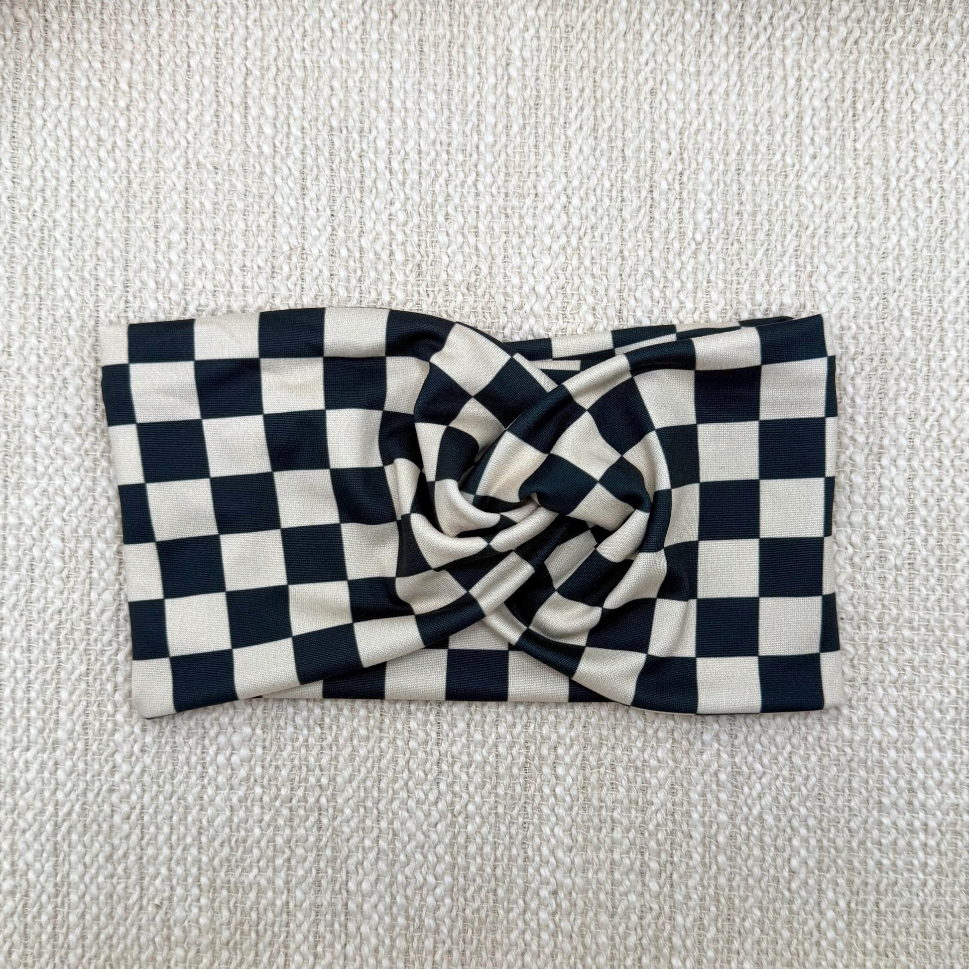 Wide, stretchy headband in black and tan checker print displayed on a cream color background.