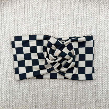 Wide, stretchy headband in black and tan checker print displayed on a cream color background.