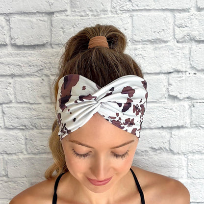 Woman with hair in ponytail wearing wide, twisted headband with cow print.