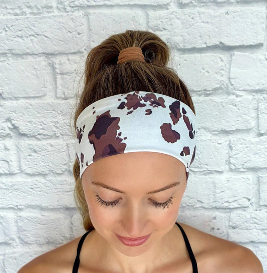 Woman with hair in ponytail wearing flat, stretchy headband in white with cow print.