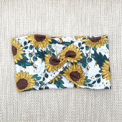 Wide, stretchy headband in white with yellow sunflower print displayed on a cream color background.