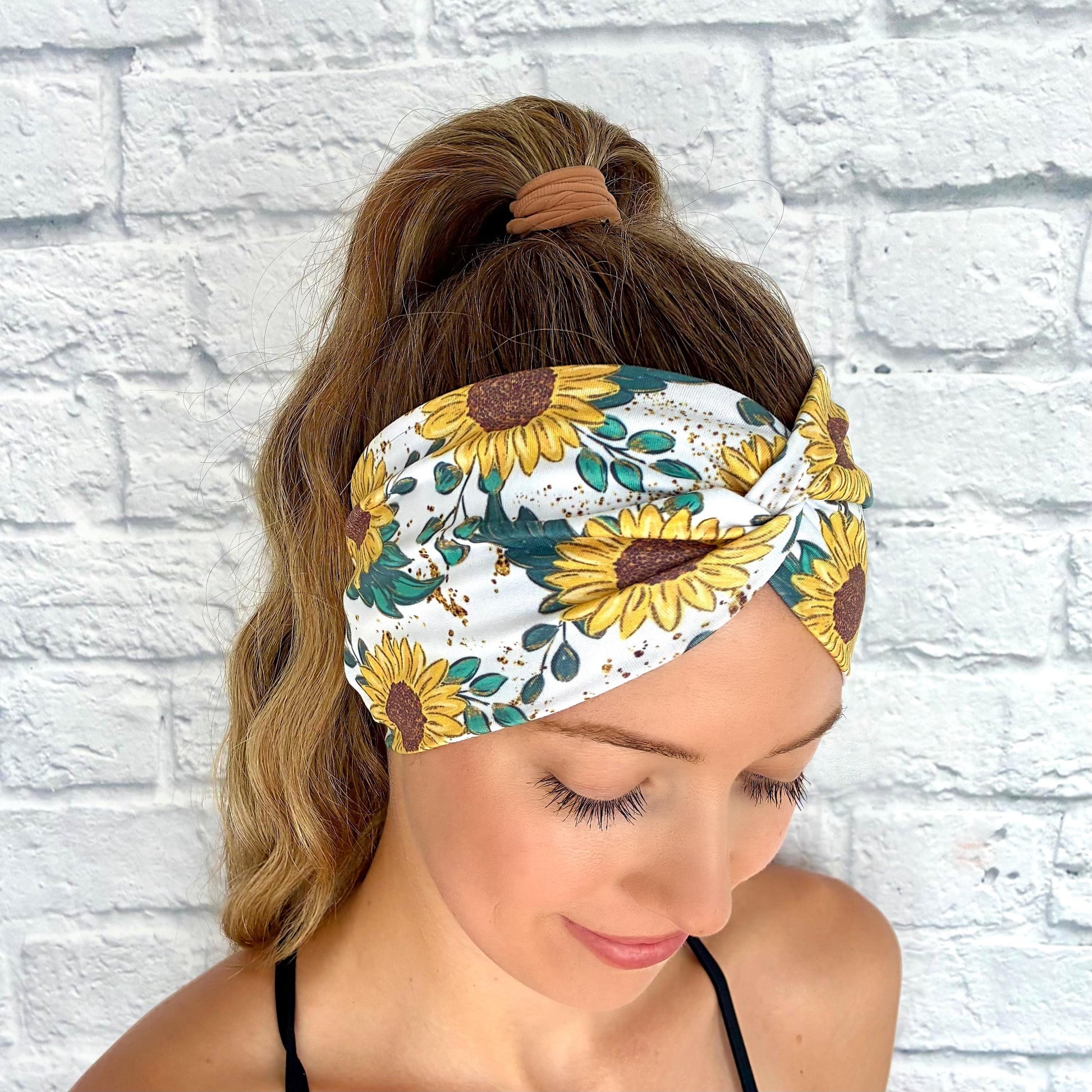 Woman with hair in ponytail wearing white, stretchy headband in white with yellow sunflower print.