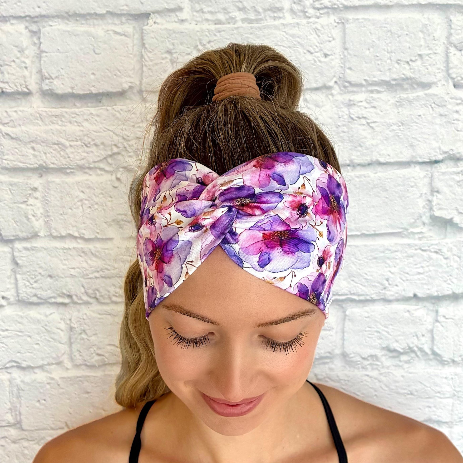 Woman with hair in ponytail wearing wide, twisted, stretchy headband with purple floral print.