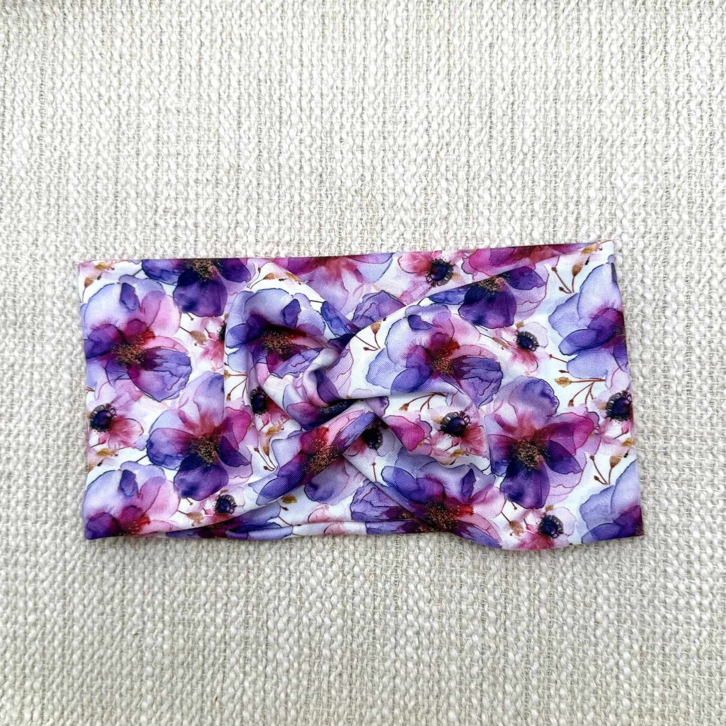 Wide, twisted, stretchy headband with purple floral print displayed on a cream color background.