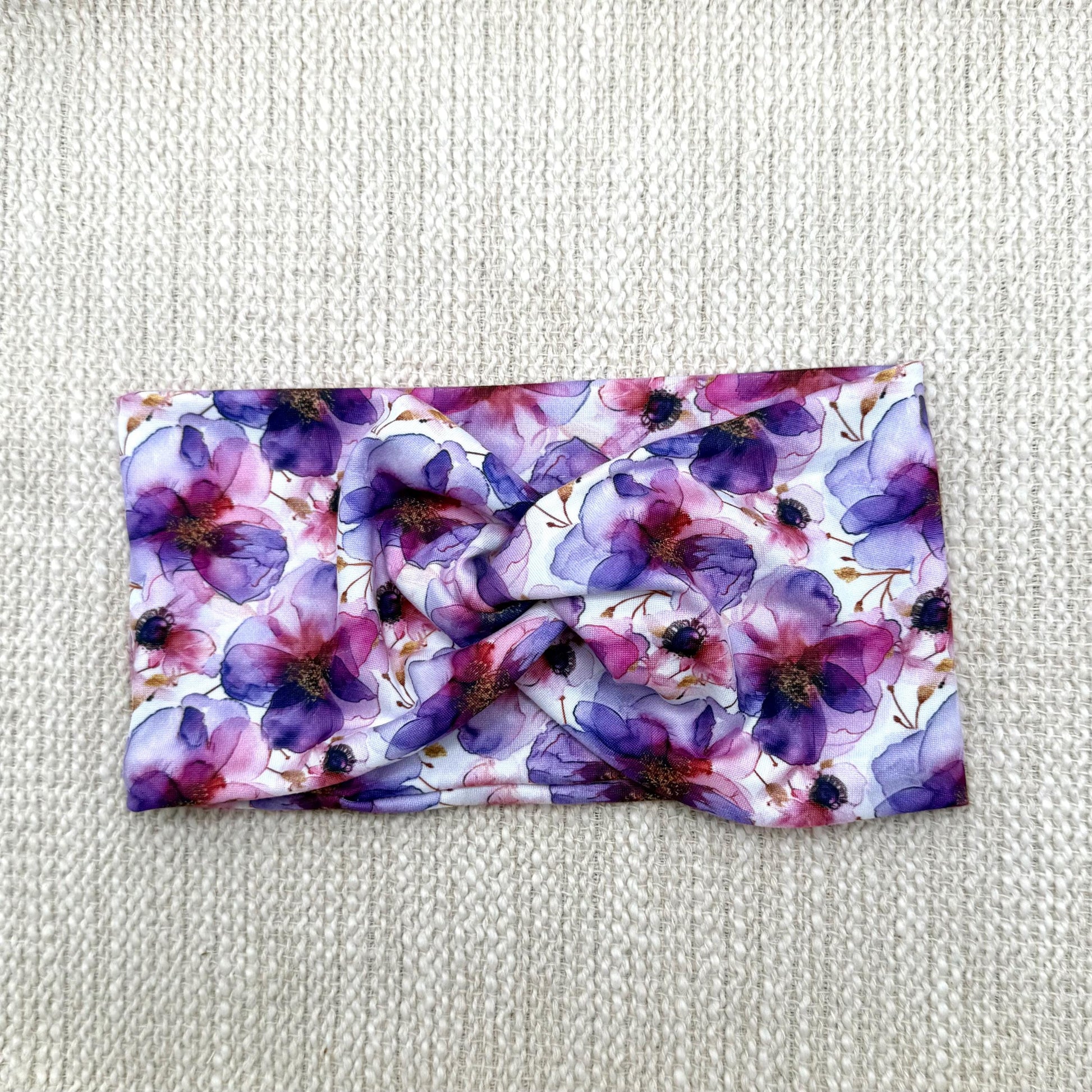 Wide, twisted, stretchy headband with purple floral print displayed on a cream color background.