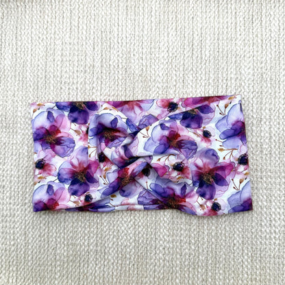 Wide, twisted, stretchy headband with purple floral print displayed on a cream color background.