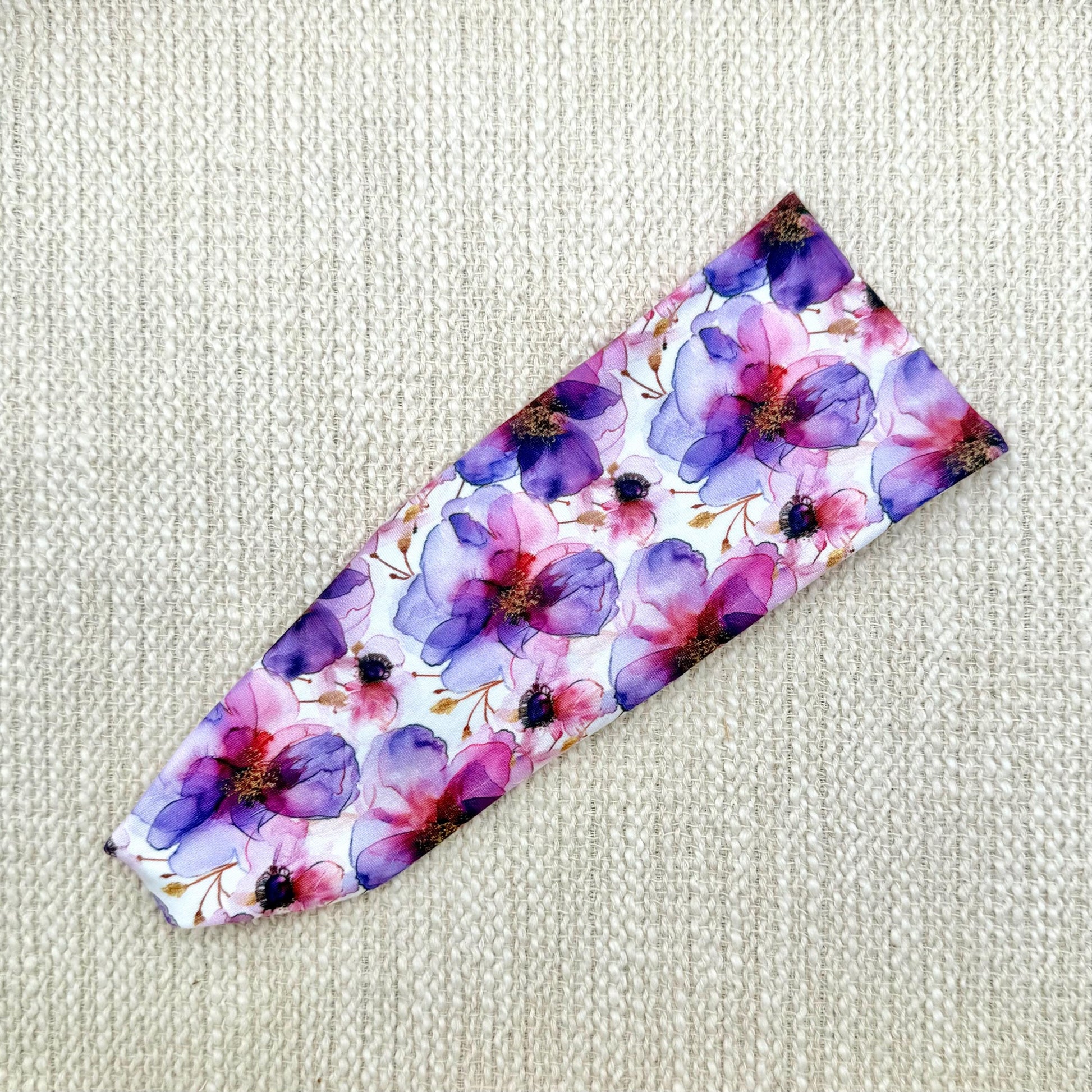 Flat, stretchy headband with purple floral print displayed on a cream color background.