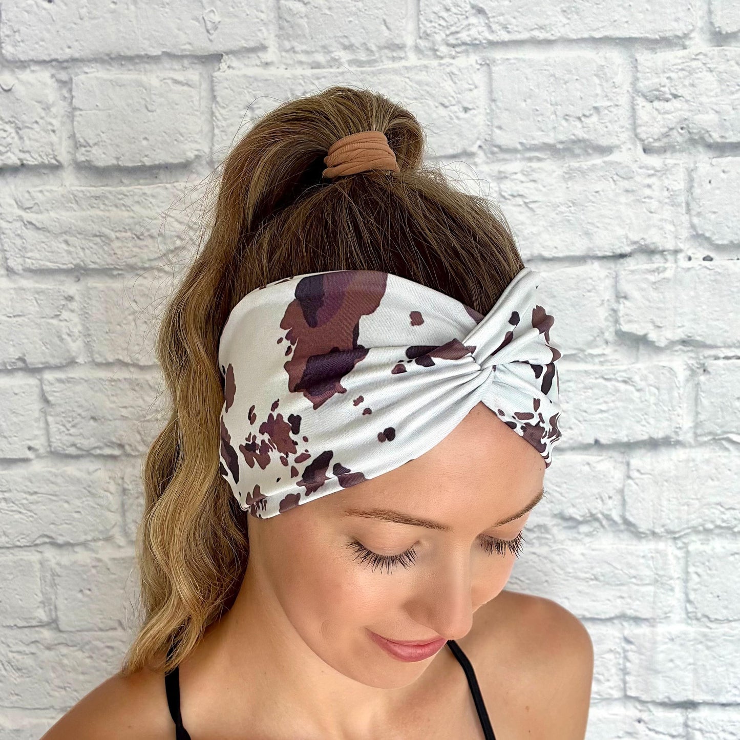 Woman with hair in ponytail wearing wide, twisted headband with cow print.