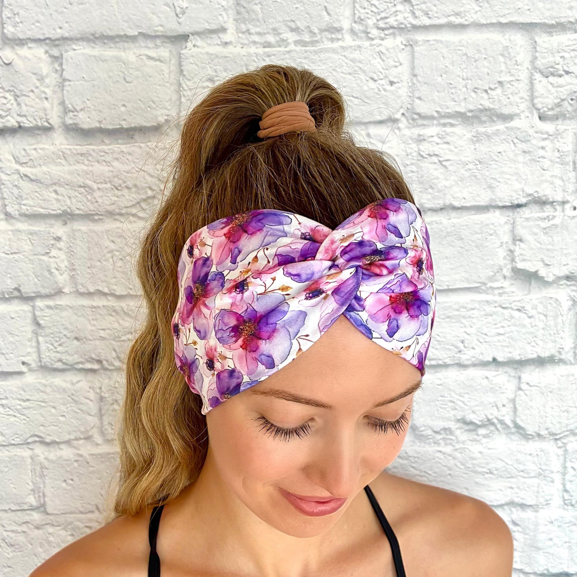 Woman with hair in ponytail wearing wide, twisted, stretchy headband with purple floral print.