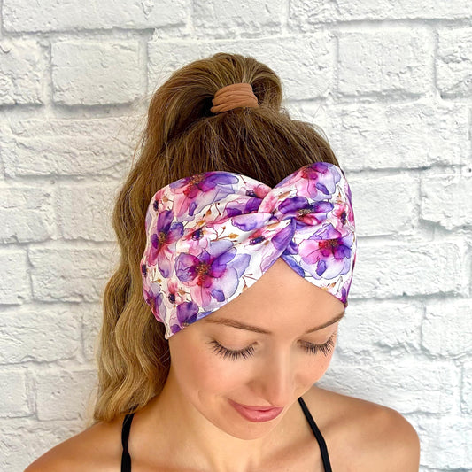 Woman with hair in ponytail wearing wide, twisted, stretchy headband with purple floral print.