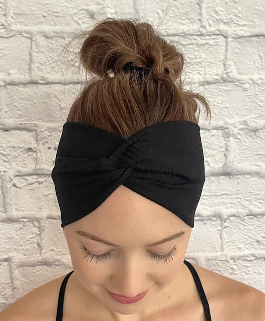 Woman with hair in bun wearing wide, twisted headband in black ribbed print.
