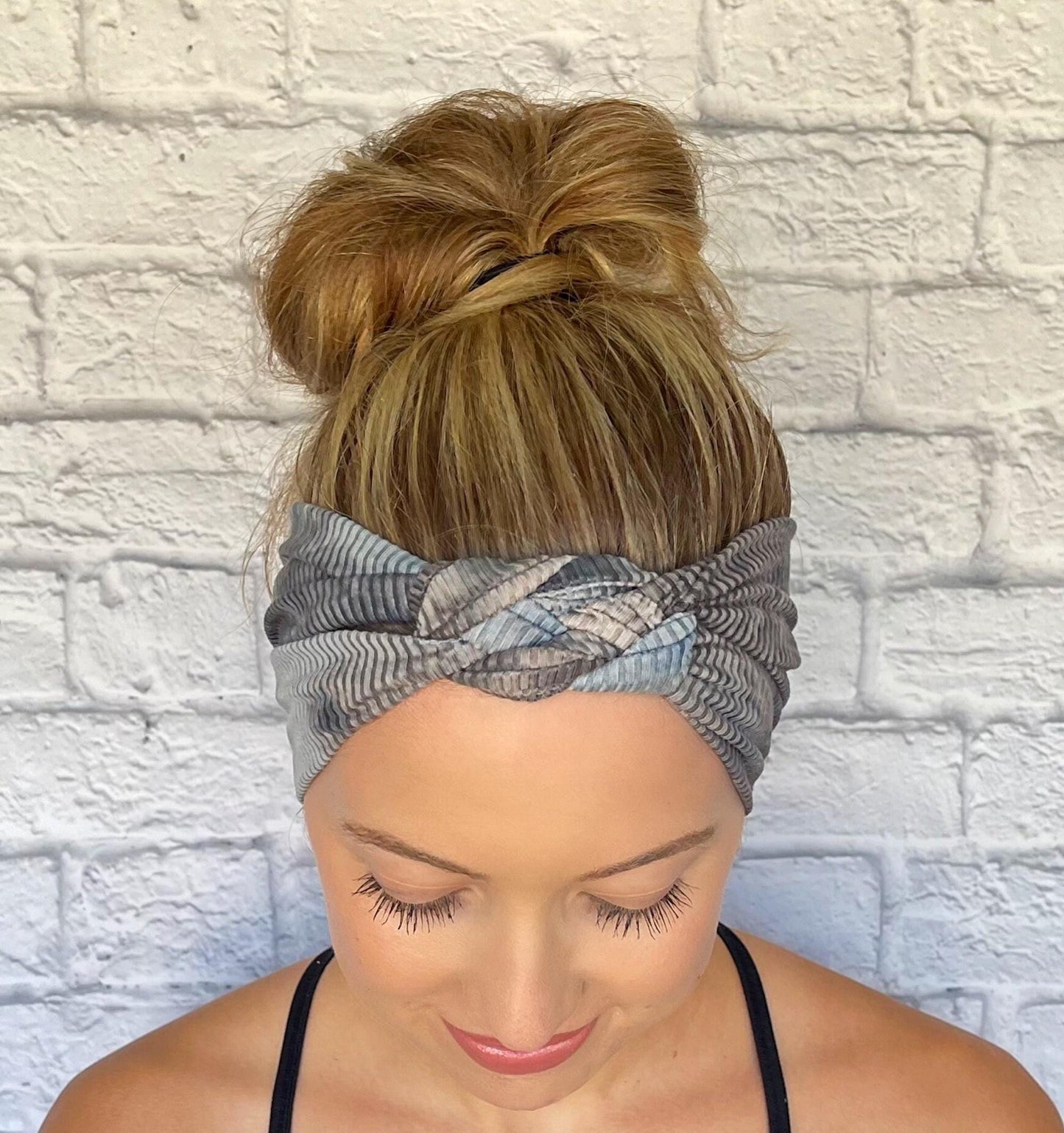 Woman with hair in bun wearing sailor knot style headband in ribbed fabric with gray and blue tie dye print.