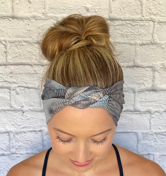 Woman with hair in bun wearing sailor knot style headband in ribbed fabric with gray and blue tie dye print.