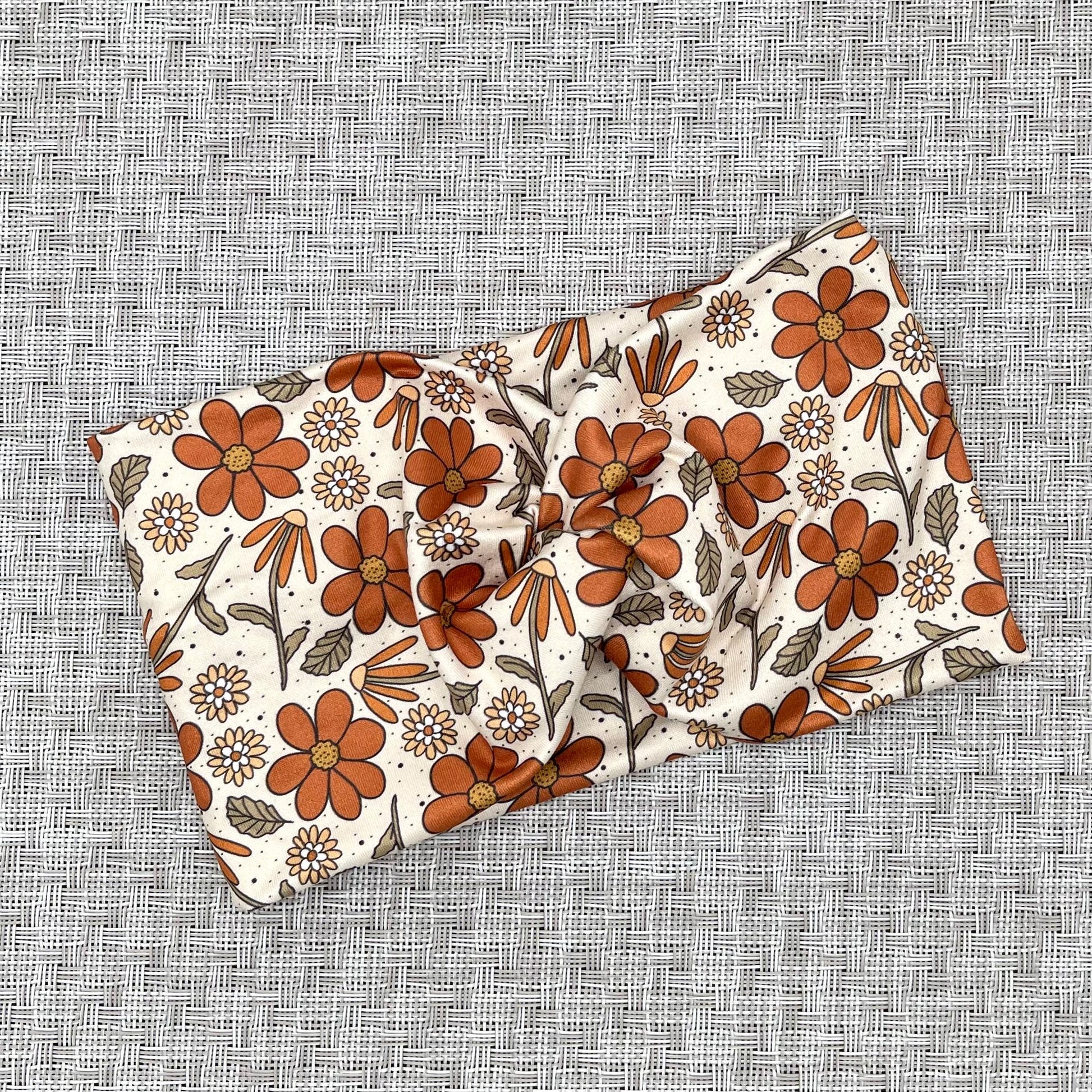 Wide, twisted headband with burnt orange and yellow color floral print.