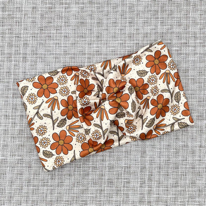 Wide, twisted headband with burnt orange and yellow color floral print.