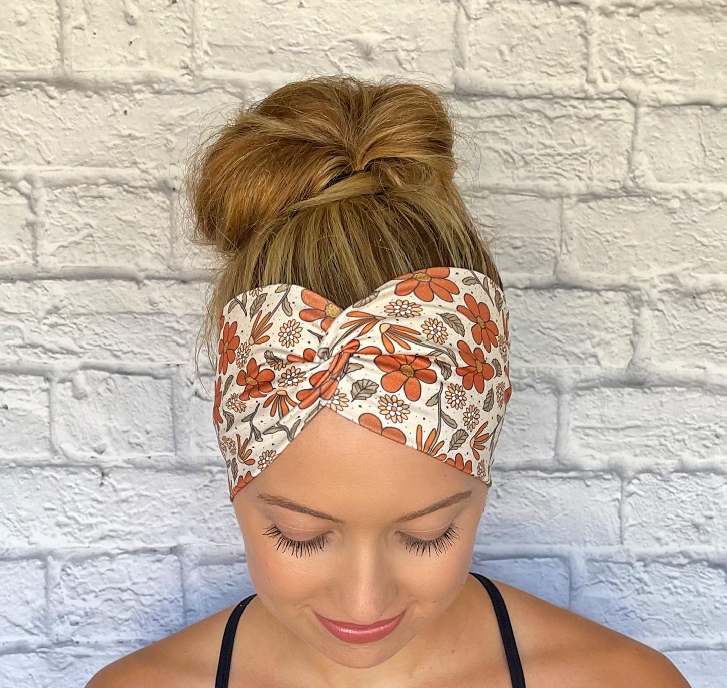 Woman with hair in bun wearing wide, twisted headband with burnt orange and yellow color floral print.
