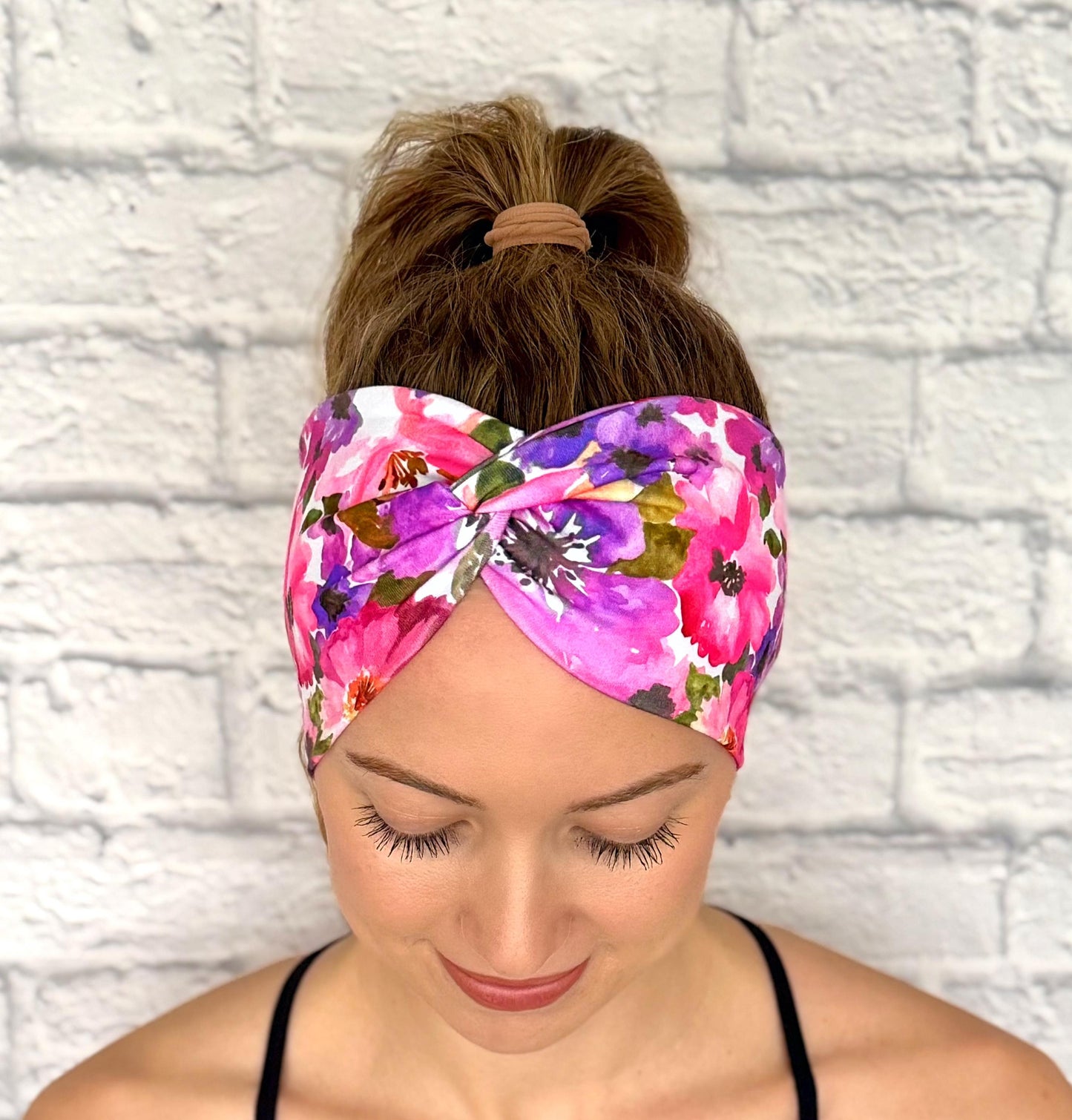 Woman with hair in ponytail wearing wide, twisted, stretchy headband with purple floral print.