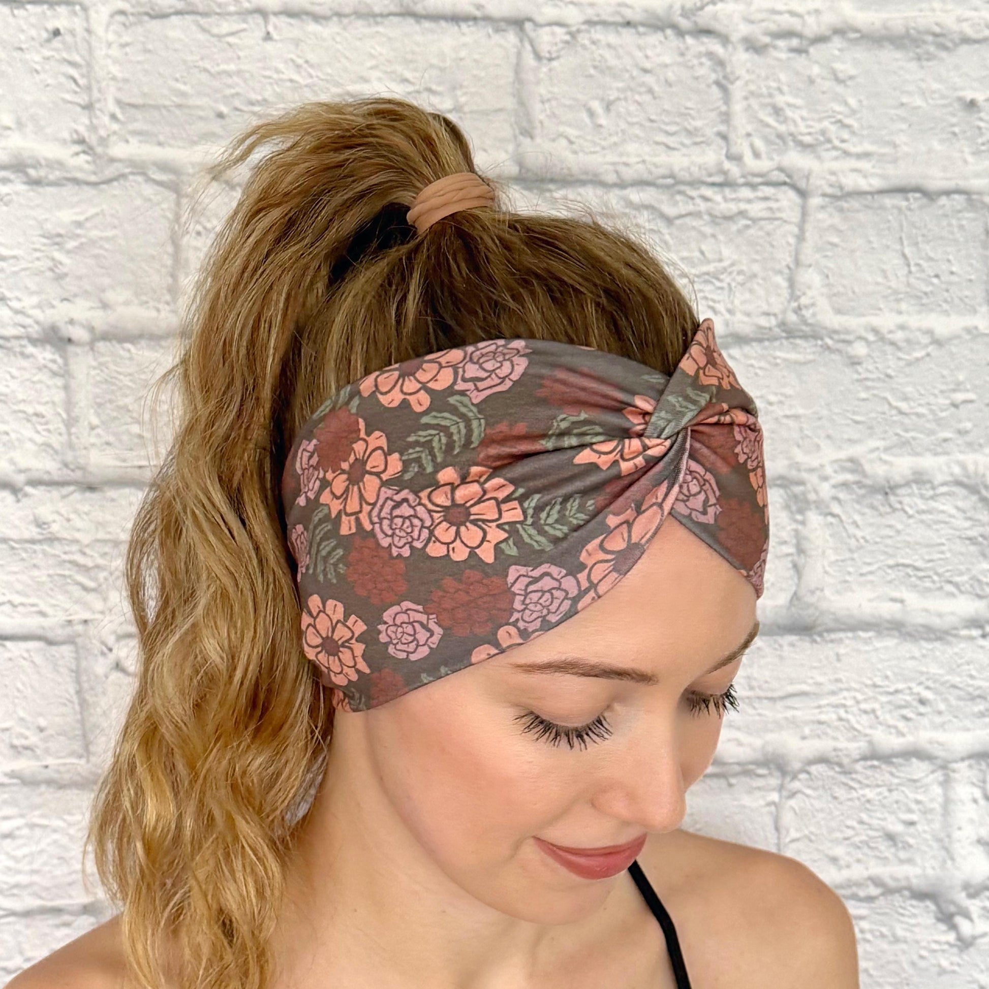 Woman with hair in ponytail wearing wide, twisted headband in gray/brown with peach color floral print.