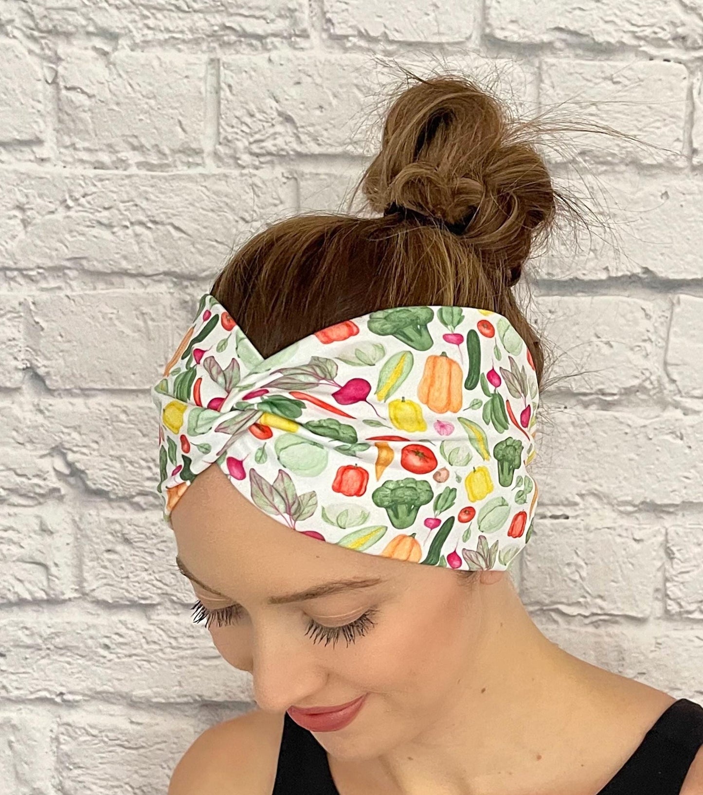 Woman with hair in bun wearing wide, twisted headband in white with vegetable theme print.