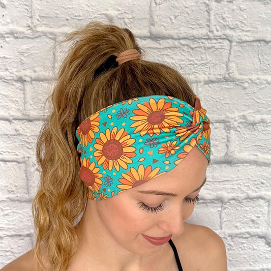Woman with hair in ponytail wearing wide, twisted headband in teal color with sunflower print.