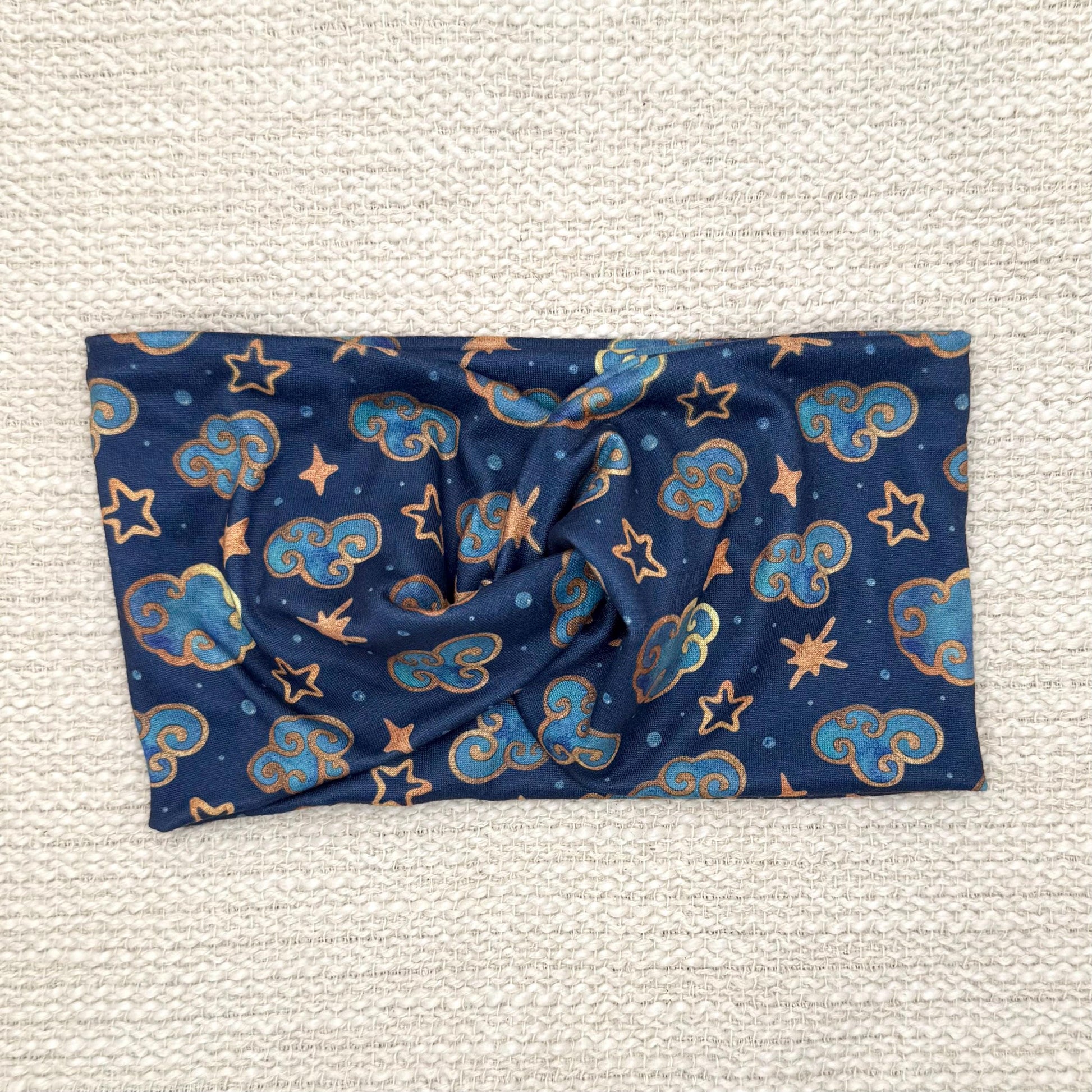 Wide, twisted headband in navy blue with clouds, stars, and space theme print.