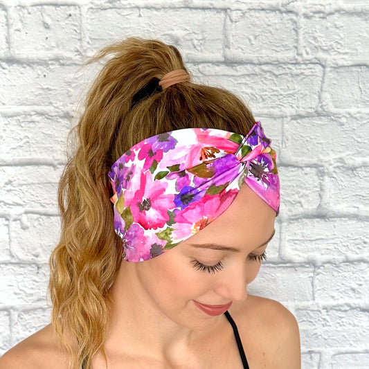 Woman with hair in ponytail wearing wide, twisted, stretchy headband with purple floral print.