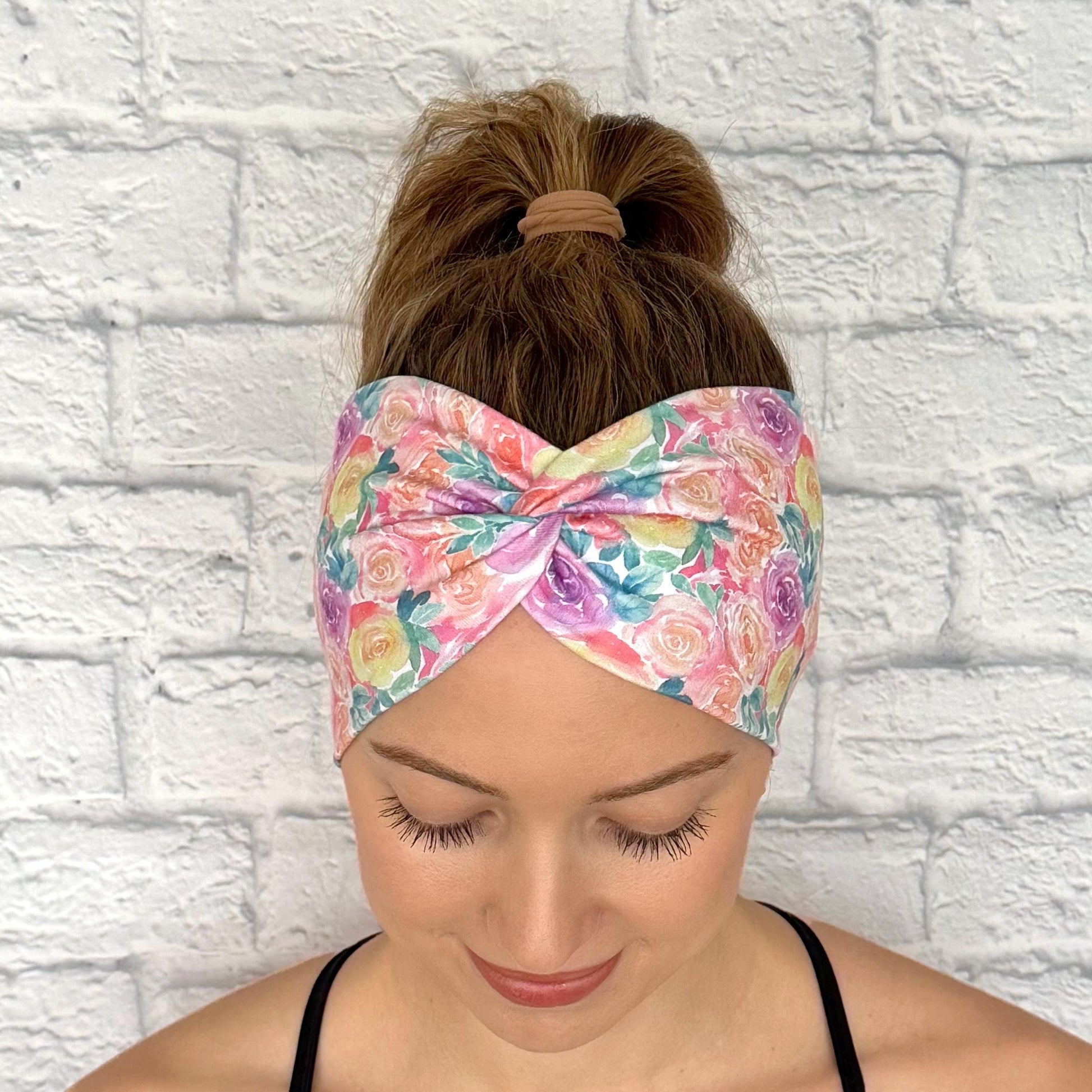 Woman with hair in curled ponytail wearing wide, twisted headband in pastel color rose print.