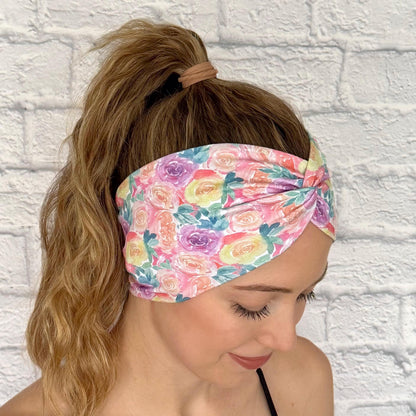 Woman with hair in curled ponytail wearing wide, twisted headband in pastel color rose print.