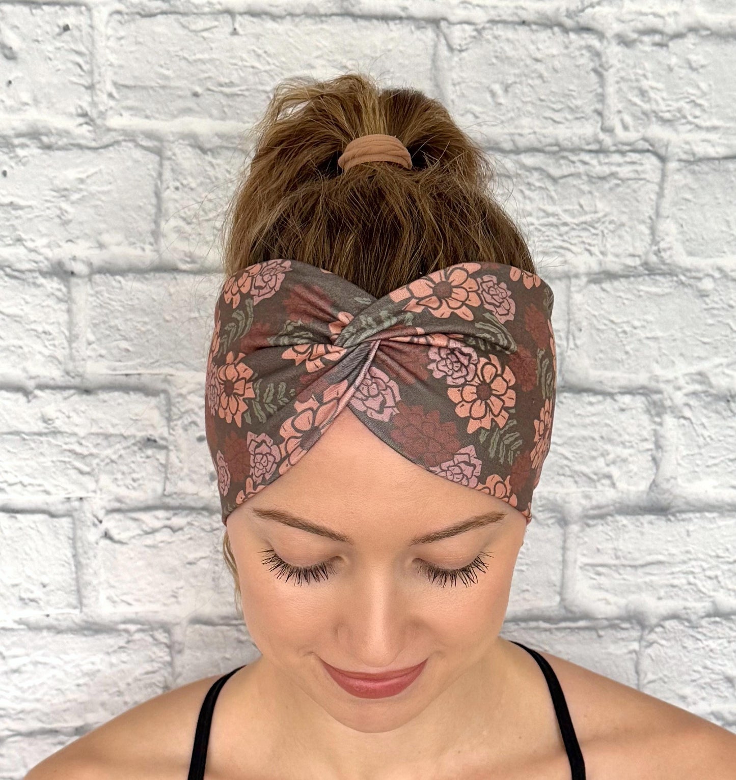 Woman with hair in ponytail wearing wide, twisted headband in gray/brown with peach color floral print.