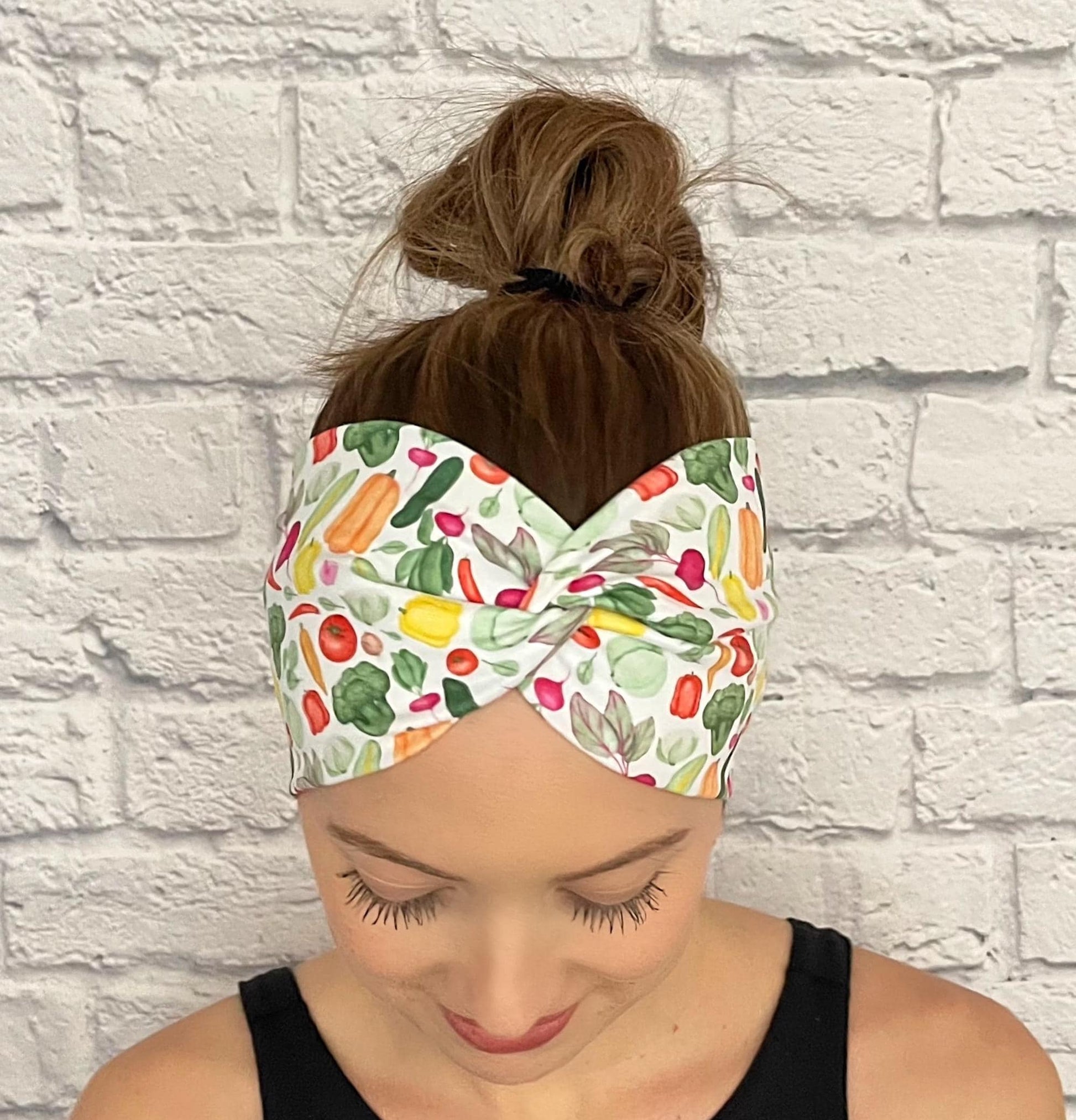 Woman with hair in bun wearing wide, twisted headband in white with vegetable theme print.