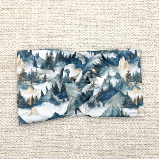 Wide, twisted headband with mountain print in varying shades of blue and tan.